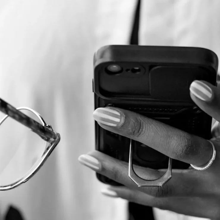 Foto in bianco e nero di una persona che consulta lo smartphone tenendo gli occhiali nell'altra mano