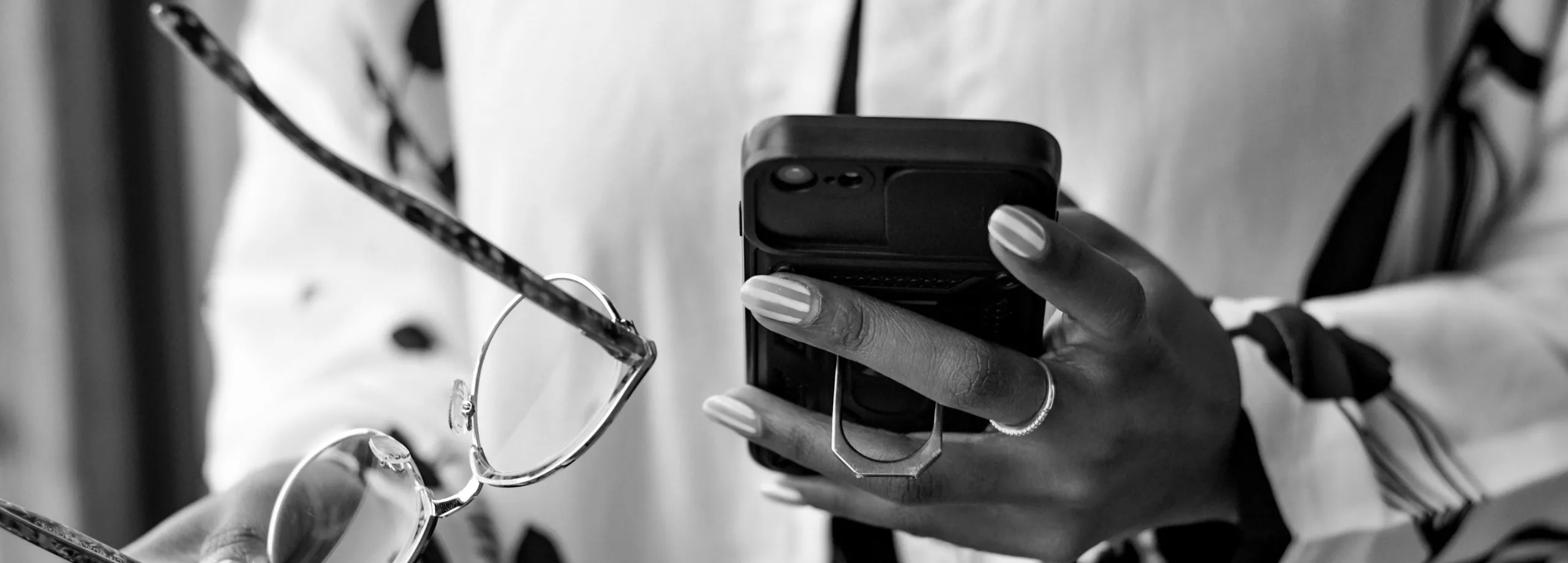 Foto in bianco e nero di una persona che consulta lo smartphone tenendo gli occhiali nell'altra mano