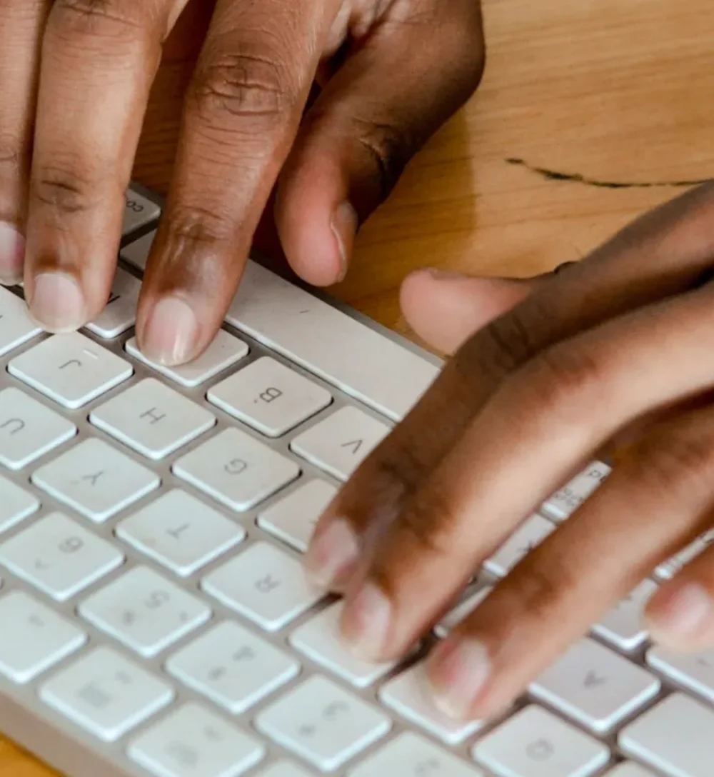 Mani che digitano su una tastiera bianca appoggiata a una scrivania in legno