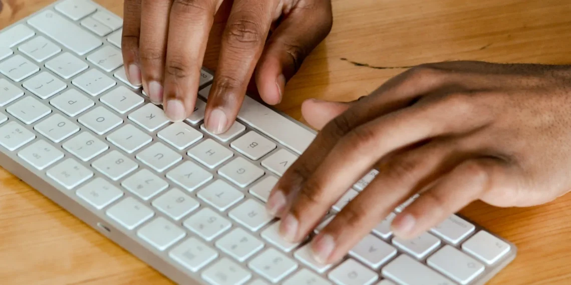 Mani che digitano su una tastiera bianca appoggiata a una scrivania in legno