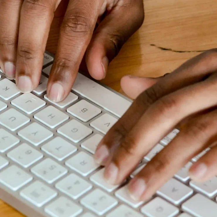 Mani che digitano su una tastiera bianca appoggiata a una scrivania in legno