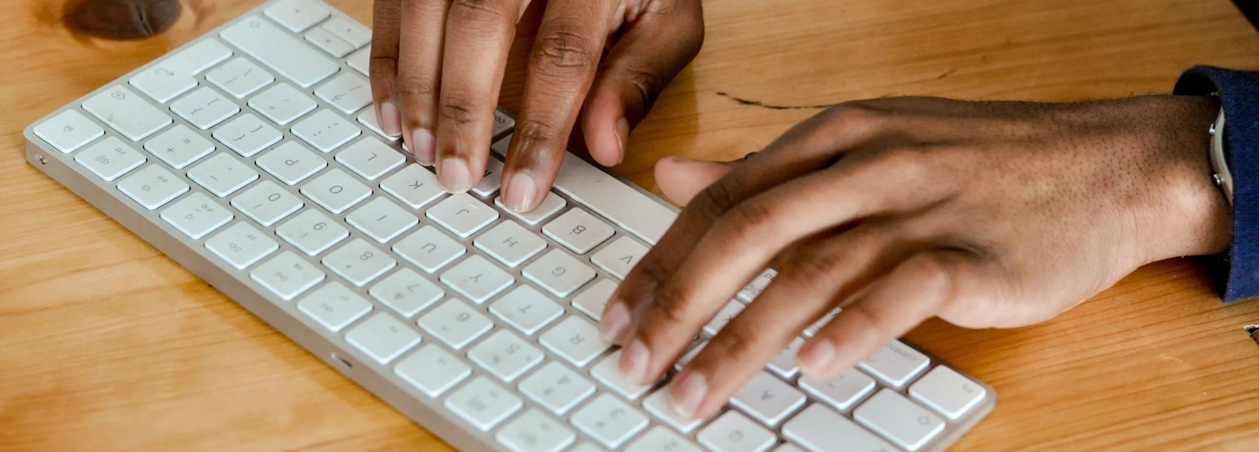 Mani che digitano su una tastiera bianca appoggiata a una scrivania in legno