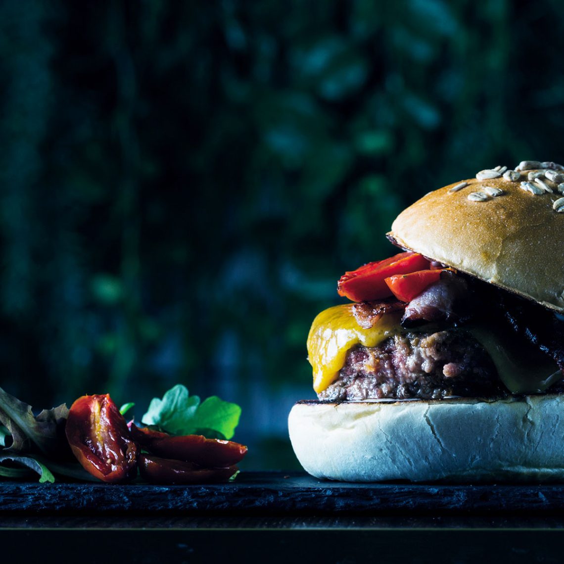 Hamburger gourmet servito su un tagliere di ardesia con pomodorini confit e insalata